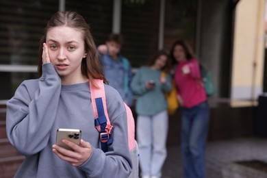Photo of Teenage girl with smartphone suffering from bullying at school, selective focus