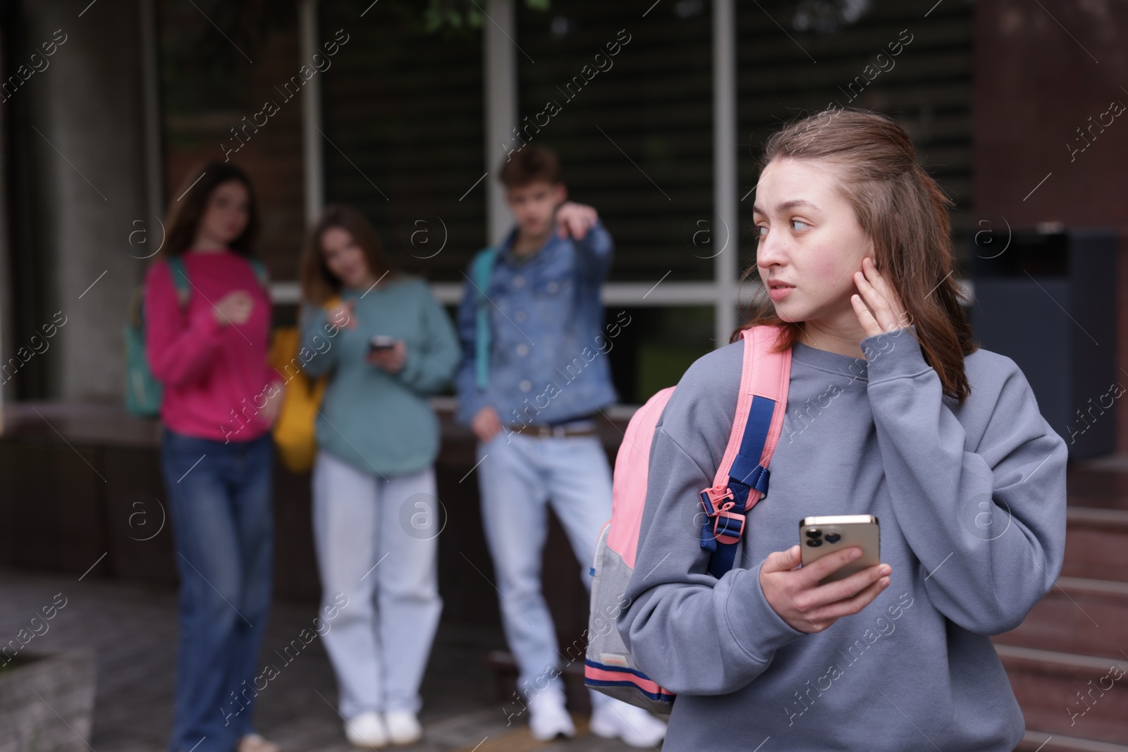 Teenage girl with smartphone suffering from bullying at school, selective focus Photo of Teenage girl with smartphone suffering from bullying at school, selective focus