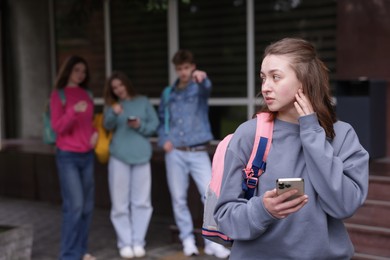 Photo of Teenage girl with smartphone suffering from bullying at school, selective focus