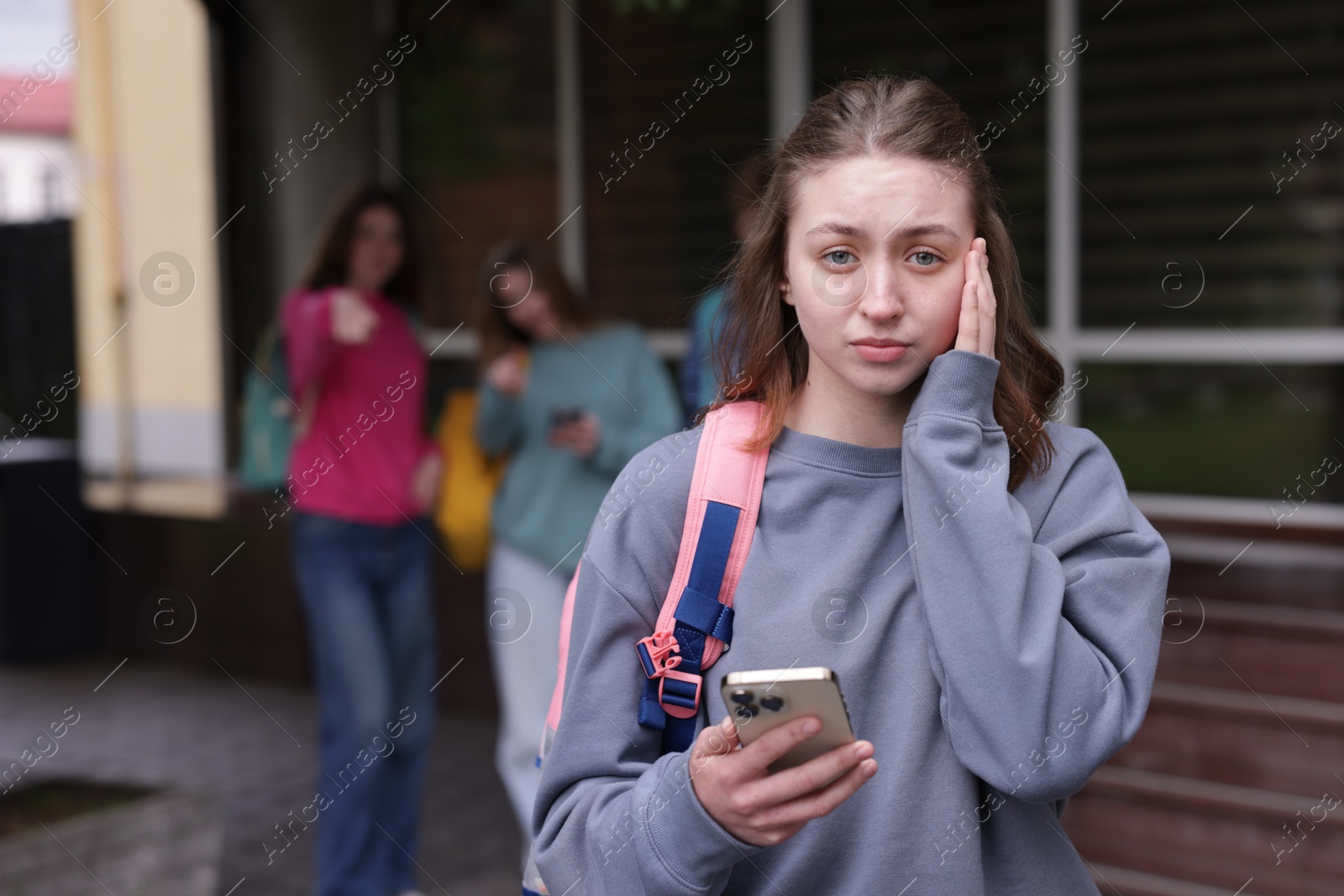 Teenage girl with smartphone suffering from bullying at school, selective focus Photo of Teenage girl with smartphone suffering from bullying at school, selective focus