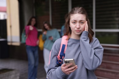 Photo of Teenage girl with smartphone suffering from bullying at school, selective focus