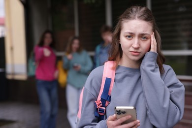 Photo of Teenage girl with smartphone suffering from bullying at school, selective focus