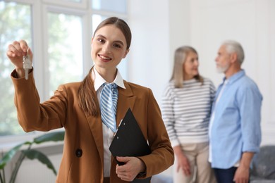 Photo of Smiling real estate agent with clipboard, house key and couple at home, selective focus