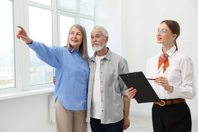 Photo of Smiling real estate agent with clipboard and couple at home