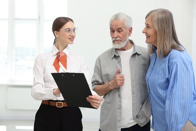 Photo of Smiling real estate agent with clipboard working with couple at home