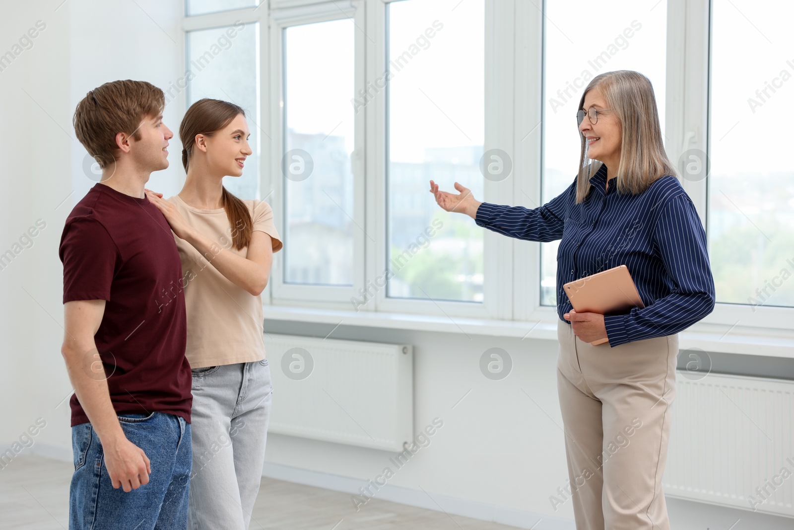 Smiling real estate agent with tablet showing apartment to couple indoors Photo of Smiling real estate agent with tablet showing apartment to couple indoors