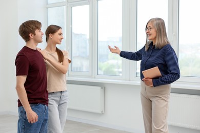 Photo of Smiling real estate agent with tablet showing apartment to couple indoors