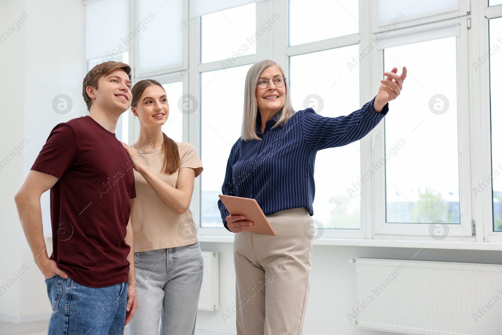 Smiling real estate agent with tablet showing apartment to couple indoors, low angle view Photo of Smiling real estate agent with tablet showing apartment to couple indoors, low angle view