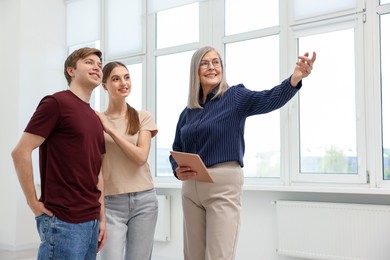 Photo of Smiling real estate agent with tablet showing apartment to couple indoors, low angle view