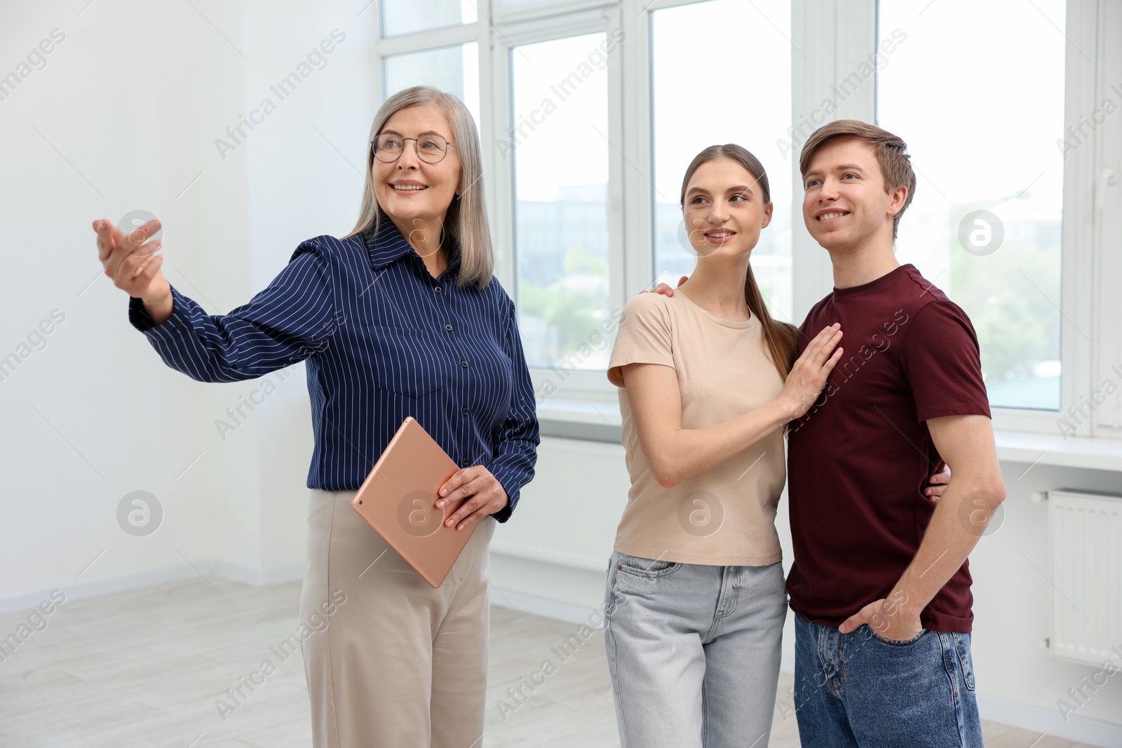 Smiling real estate agent with tablet showing apartment to couple indoors Photo of Smiling real estate agent with tablet showing apartment to couple indoors
