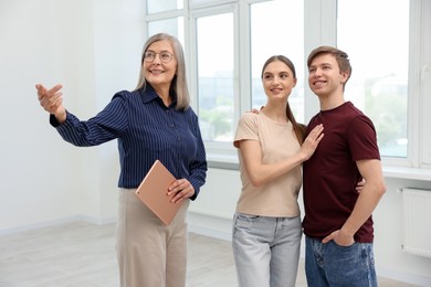Photo of Smiling real estate agent with tablet showing apartment to couple indoors