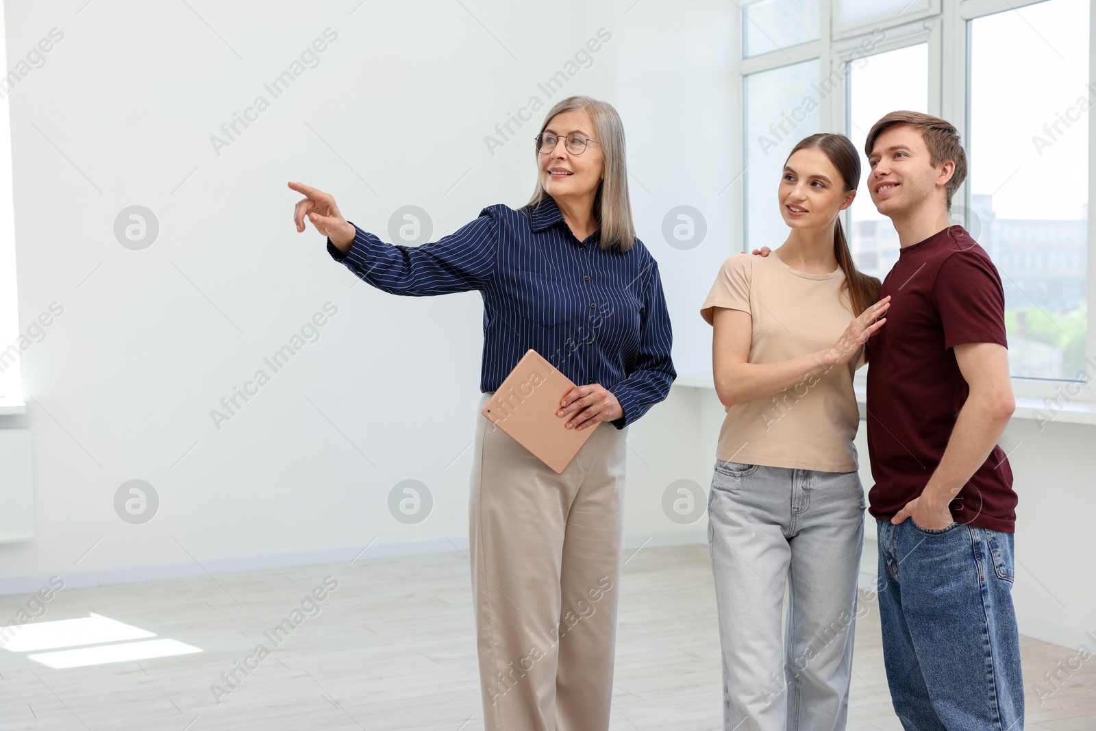 Smiling real estate agent with tablet showing apartment to couple indoors. Space for text Photo of Smiling real estate agent with tablet showing apartment to couple indoors. Space for text