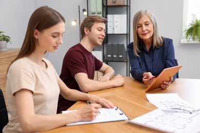 Photo of Real estate agent with tablet working with couple at table in office