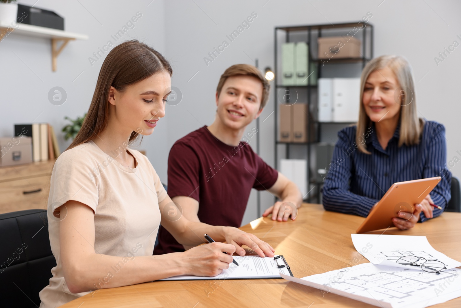 Real estate agent and couple doing paperwork at table in office, selective focus Photo of Real estate agent and couple doing paperwork at table in office, selective focus