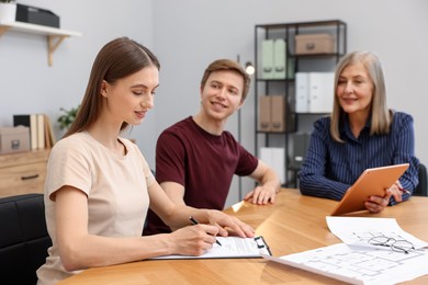 Photo of Real estate agent and couple doing paperwork at table in office, selective focus