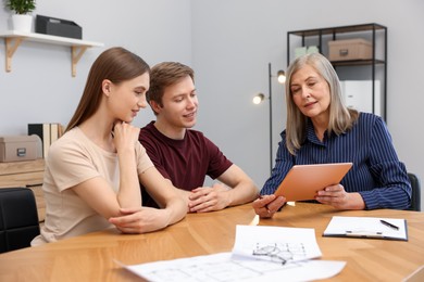Photo of Real estate agent with tablet working with couple at table in office