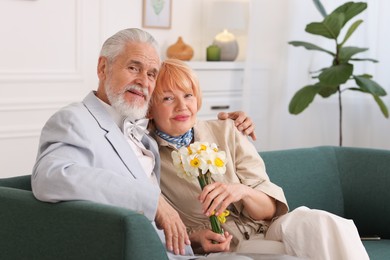 Photo of Lovely senior couple with bouquet of flowers on sofa at home