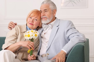 Photo of Lovely senior couple with bouquet of flowers on sofa at home