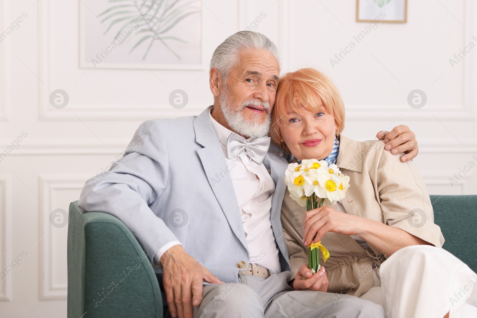 Lovely senior couple with bouquet of flowers on sofa at home Photo of Lovely senior couple with bouquet of flowers on sofa at home