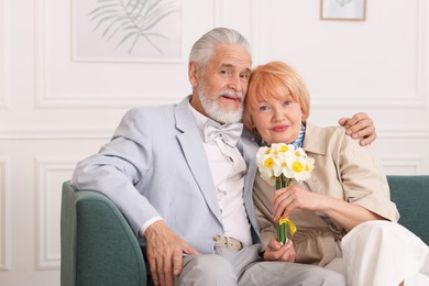 Photo of Lovely senior couple with bouquet of flowers on sofa at home