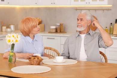 Photo of Lovely senior couple having breakfast together at wooden table in kitchen