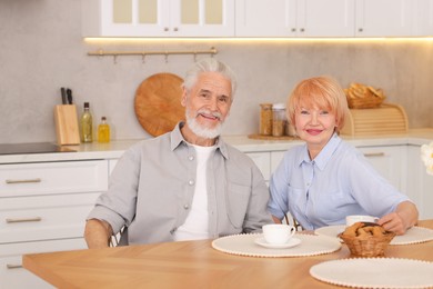 Photo of Lovely senior couple having breakfast together at wooden table in kitchen