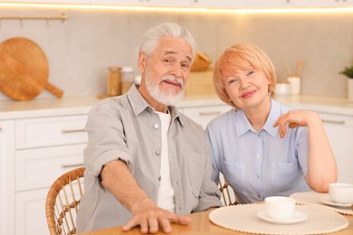Photo of Lovely senior couple having breakfast together at wooden table in kitchen