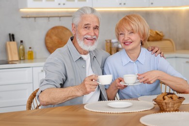 Photo of Lovely senior couple having breakfast together at wooden table in kitchen