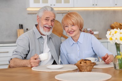 Photo of Lovely senior couple having breakfast together at wooden table in kitchen