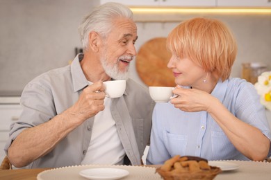 Photo of Lovely senior couple having breakfast together at wooden table in kitchen