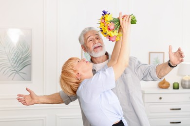 Photo of Lovely senior couple with bouquet of flowers at home