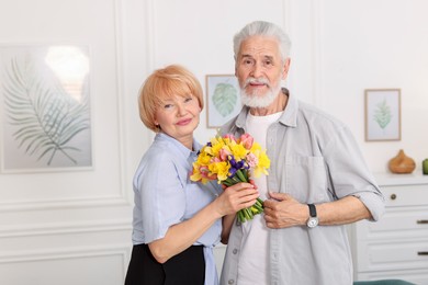 Photo of Lovely senior couple with bouquet of flowers at home