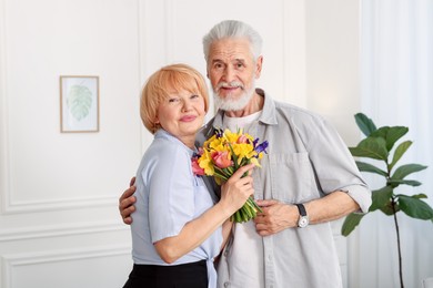 Photo of Lovely senior couple with bouquet of flowers at home
