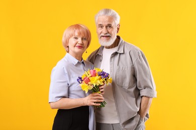 Photo of Lovely senior couple with bouquet of flowers on yellow background