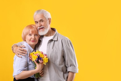 Photo of Lovely senior couple with bouquet of flowers on yellow background, space for text