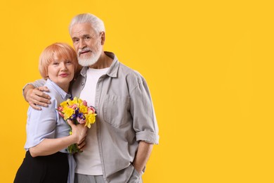 Photo of Lovely senior couple with bouquet of flowers on yellow background, space for text