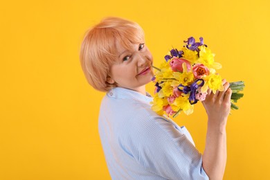 Photo of Senior woman with bouquet of flowers on yellow background