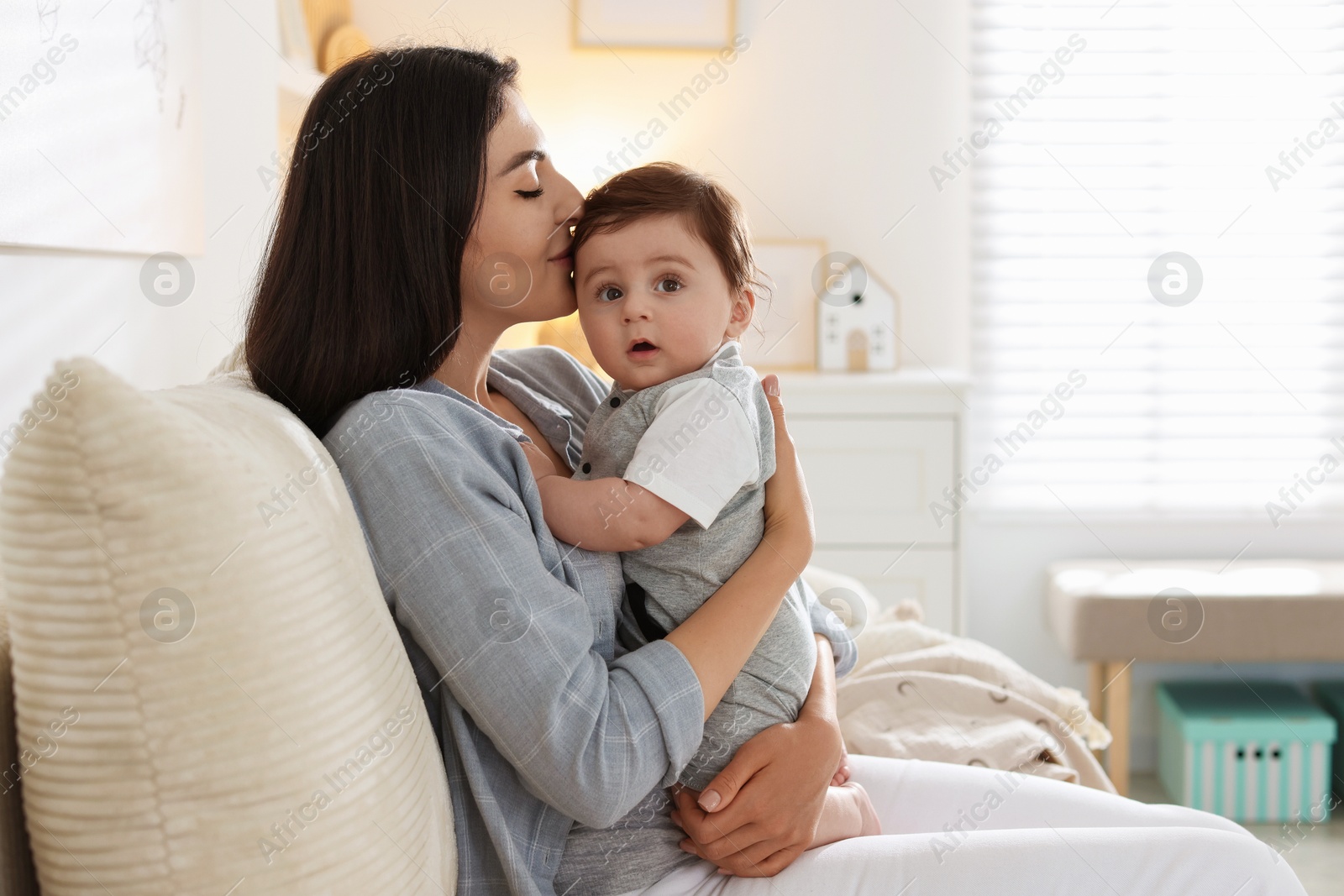 Mother kissing her cute baby on sofa at home. Space for text Photo of Mother kissing her cute baby on sofa at home. Space for text