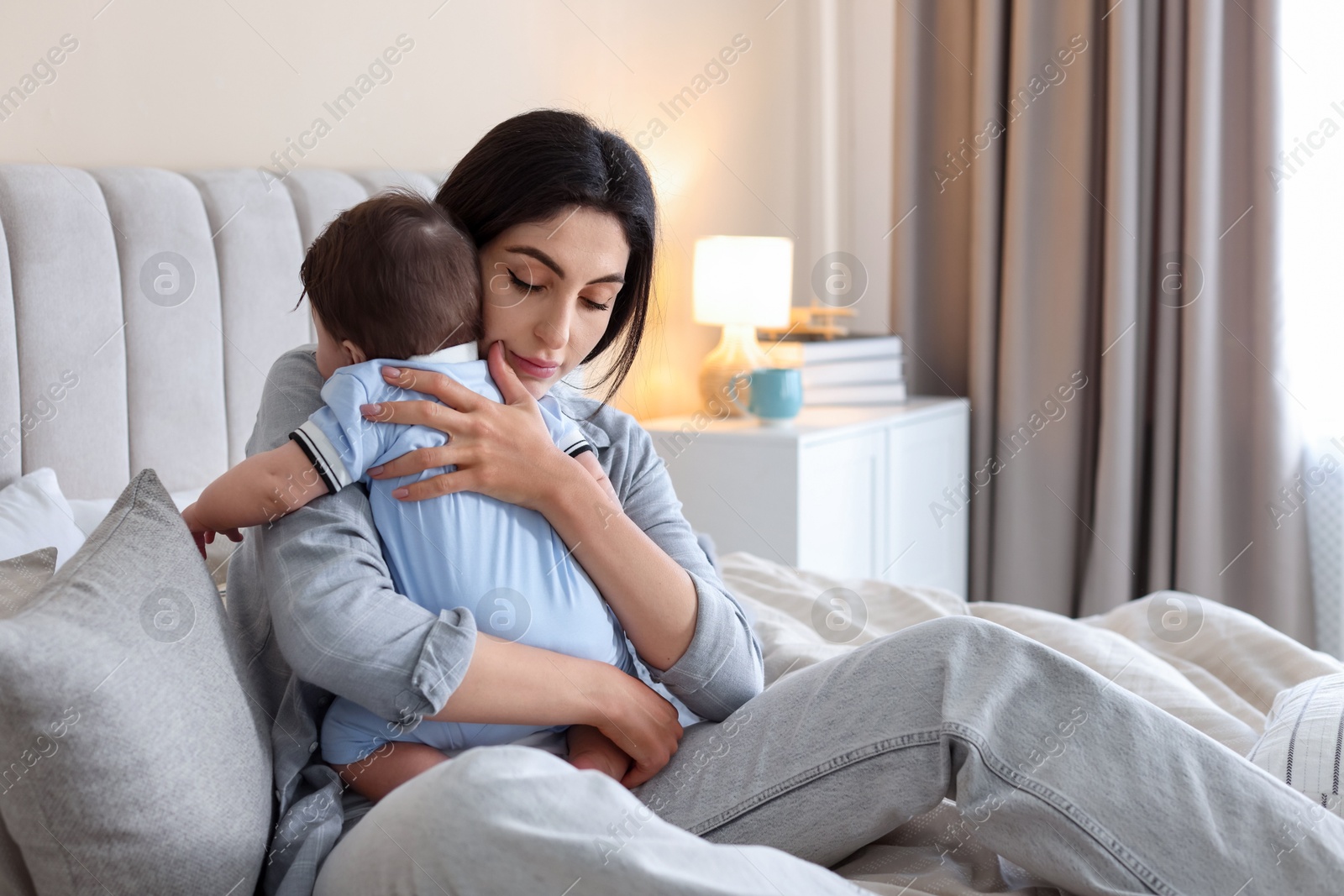 Woman suffering from postpartum depression with her little baby on bed at home. Space for text Photo of Woman suffering from postpartum depression with her little baby on bed at home. Space for text