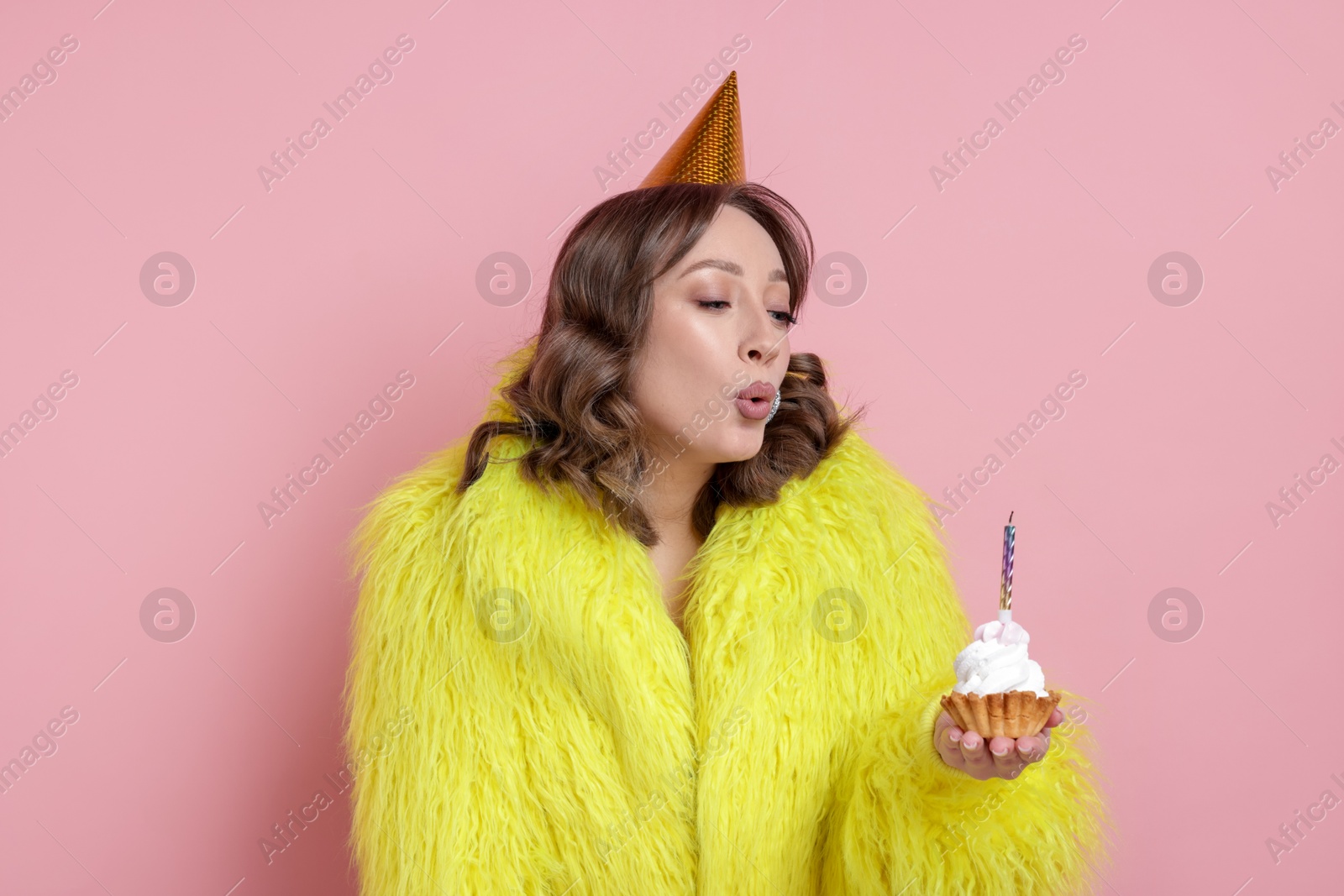 Birthday celebration. Woman blowing candle on cupcake against pink background Photo of Birthday celebration. Woman blowing candle on cupcake against pink background