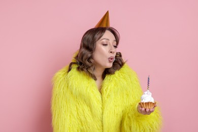 Photo of Birthday celebration. Woman blowing candle on cupcake against pink background