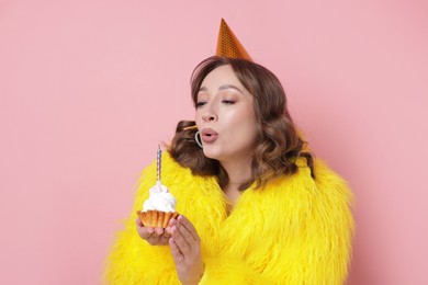 Photo of Birthday celebration. Woman blowing candle on cupcake against pink background