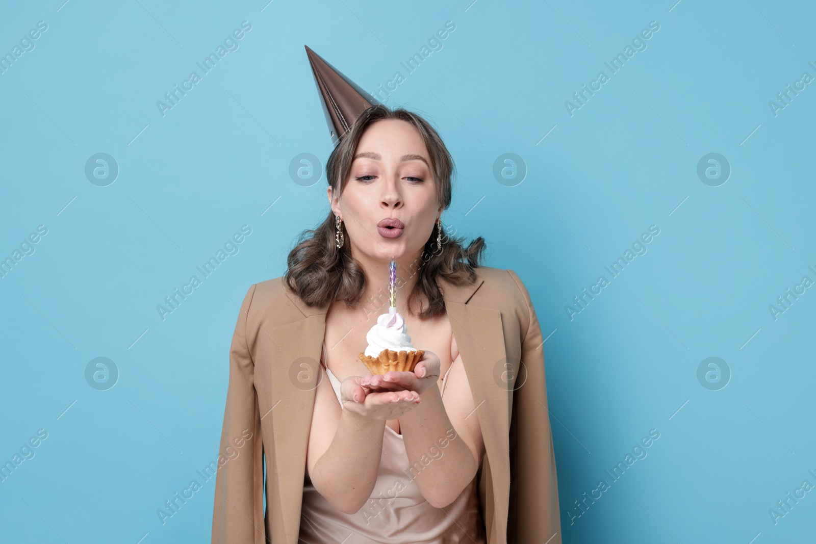 Birthday celebration. Woman blowing candle on cupcake against light blue background Photo of Birthday celebration. Woman blowing candle on cupcake against light blue background