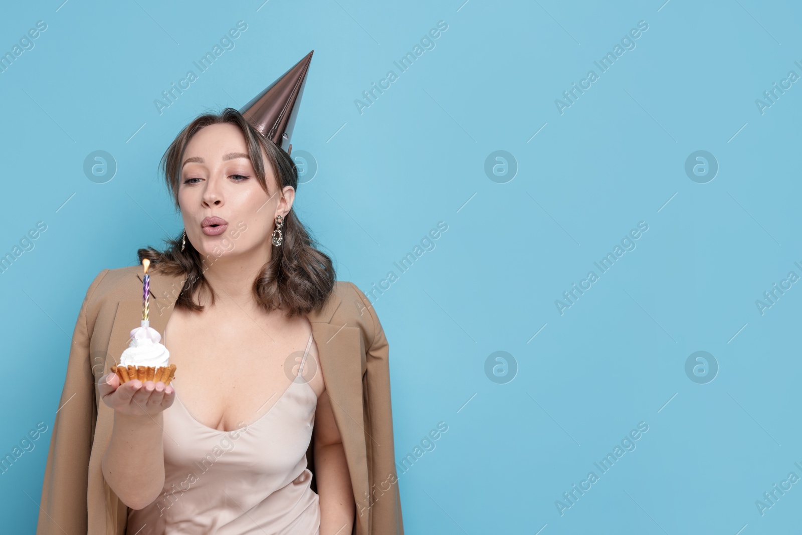 Birthday celebration. Woman blowing candle on cupcake against light blue background. Space for text Photo of Birthday celebration. Woman blowing candle on cupcake against light blue background. Space for text