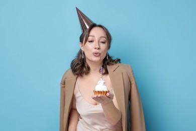 Photo of Birthday celebration. Woman blowing candle on cupcake against light blue background