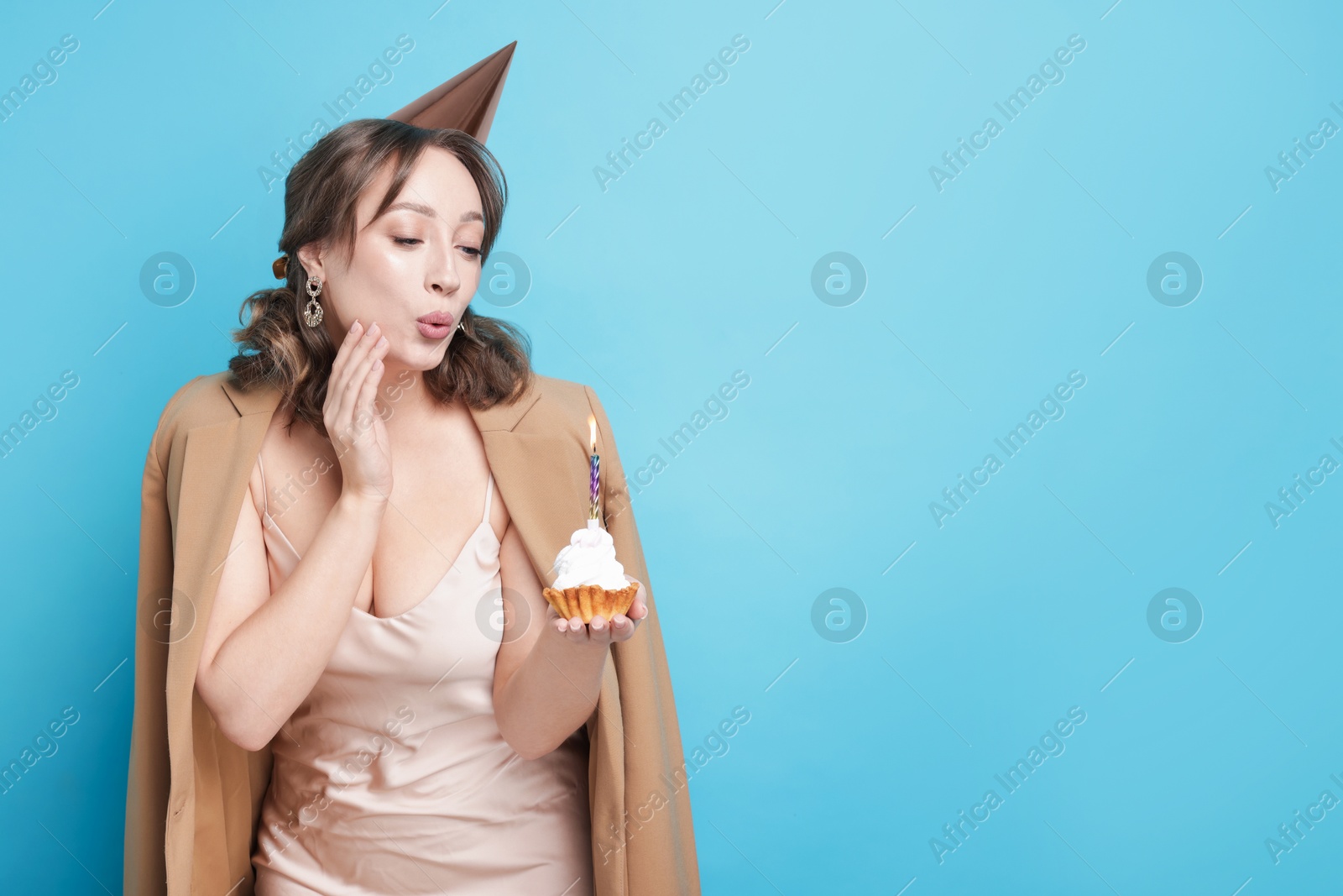Birthday celebration. Woman blowing candle on cupcake against light blue background. Space for text Photo of Birthday celebration. Woman blowing candle on cupcake against light blue background. Space for text