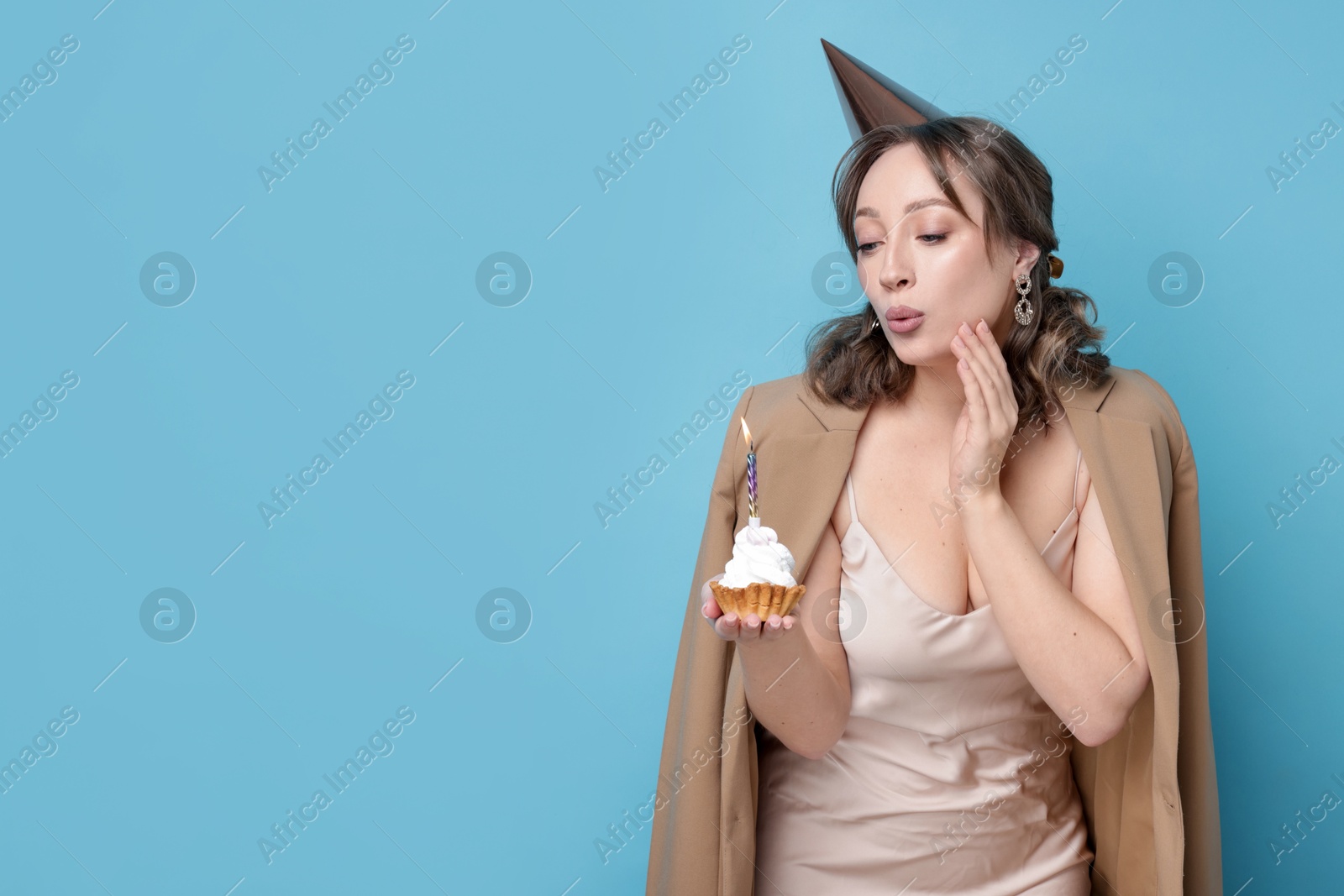 Birthday celebration. Woman blowing candle on cupcake against light blue background. Space for text Photo of Birthday celebration. Woman blowing candle on cupcake against light blue background. Space for text
