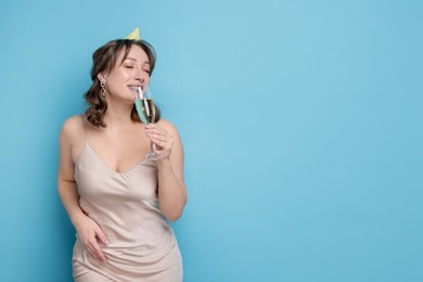Photo of Birthday celebration. Woman with glass of sparkling wine on light blue background. Space for text
