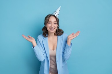 Photo of Birthday celebration. Happy woman with party cone on light blue background