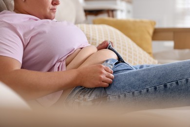 Photo of Overweight woman trying to put on tight jeans at home, closeup